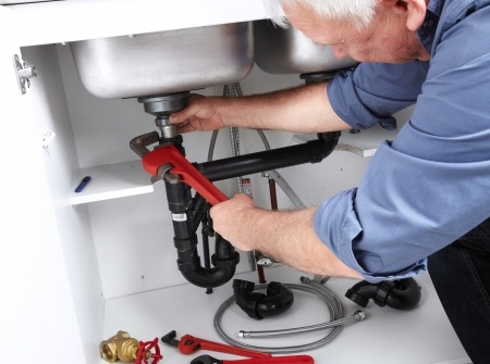 A plumber performs a commercial plumbing service on a sink.